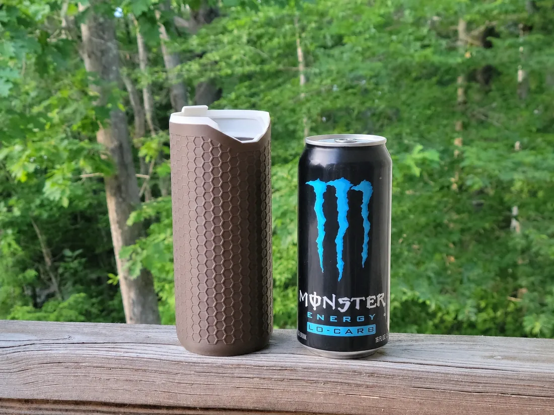 Porta-lata térmico PopTop Koozie marrom ao lado de uma lata de Monster de 568 ml