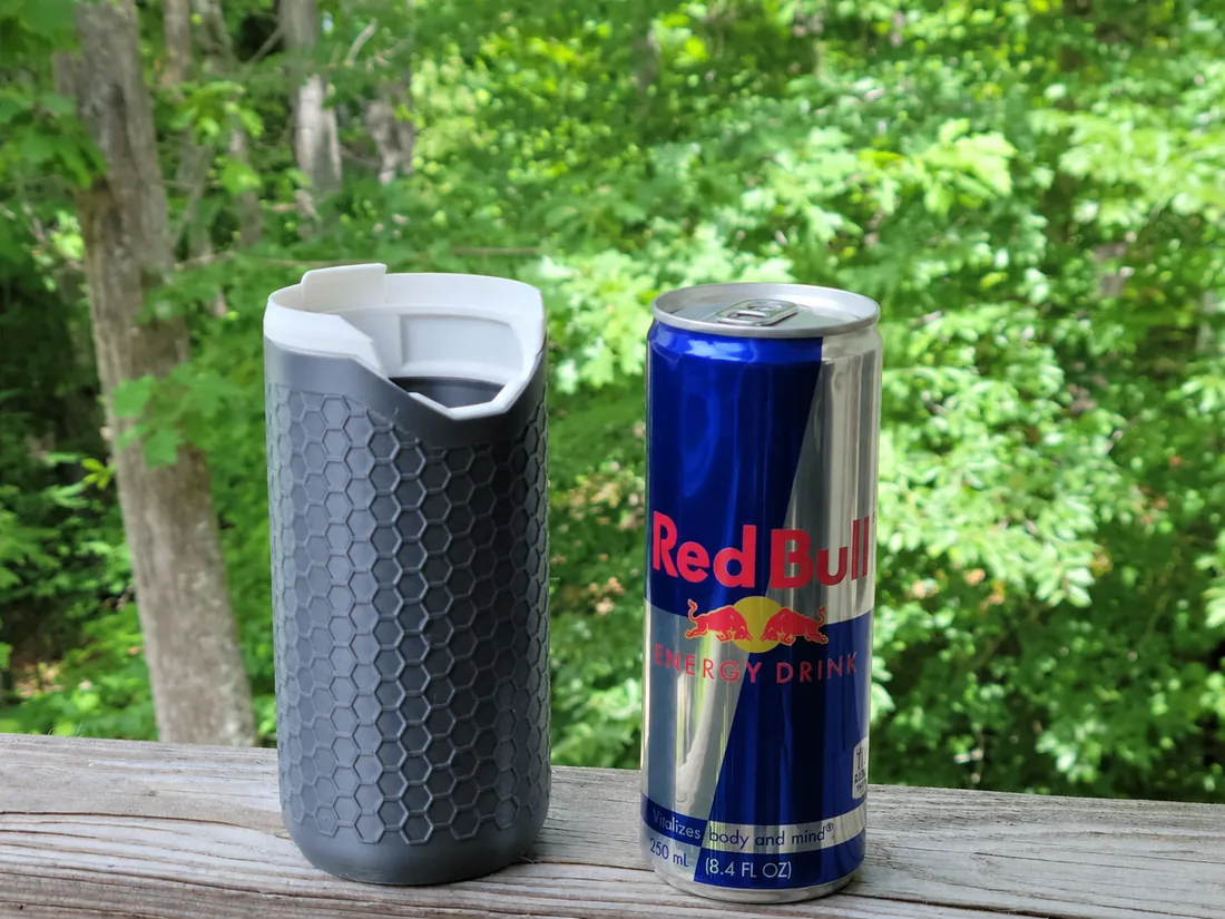 Porta-lata térmico PopTop Koozie cinza ao lado de uma latinha de Red Bull